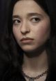 Amber Freeman from Scream 5, showcasing an intense expression, long black hair, and a silver chain necklace.