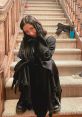 Amber Freeman poses playfully on the stairs, dressed in a stylish black outfit, embodying a modern horror vibe.