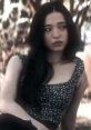 Amber from Scream V gazes pensively, showcasing her signature floral top and long dark hair in an outdoor setting.