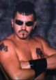 Jamie Dundee striking a confident pose, showcasing his tattoos and sunglasses, embodying the wrestling persona.