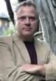 Sean Oliver poses confidently in a stylish beige blazer, surrounded by a natural outdoor setting.