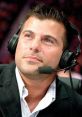 Matt Striker at the commentary table, wearing headphones and a suit, focused on the wrestling match unfolding.