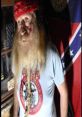 Bearded man in a red bandana stands in front of a Confederate flag, wearing a controversial graphic T-shirt.