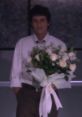 Brian Moser holding a large bouquet of white roses, dressed in a formal shirt and pants, against a minimalist background.
