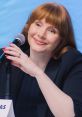 Bryce Dallas Howard speaking at a panel, showcasing her signature red hair and vibrant manicure, exuding charisma.