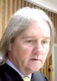 Judge Jeffrey showing a serious expression in court, emphasizing professionalism with his hat off and in formal attire.