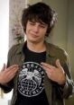 Rodrick Heffley showcasing a casual style, confident expression, and unique graphic tee in a home setting.
