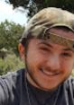 Cheerful young man wearing a camo hat and casual clothing, enjoying nature and smiling in a sunny outdoor setting.
