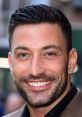 Smiling man with a short, styled haircut and a neatly groomed beard, wearing a blazer, exuding confidence and charm.