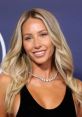 Alix Earle smiling brightly with wavy blonde hair, wearing a stylish black outfit and sparkling necklace at an event.