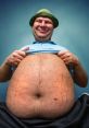 Smiling man in a blue shirt lifts his shirt, showcasing his large belly against a blue background. Lighthearted and fun.
