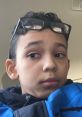 Young boy with glasses looking pensive, wearing a blue jacket in a car, showcasing a thoughtful expression.