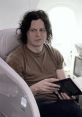 Jack White relaxing on an airplane, focused on a book, showcasing his unique style and thoughtful expression.