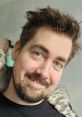 Smiling English male with short, styled hair and a cat draped over his shoulder, exuding warmth and friendliness.
