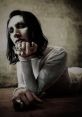 Marilyn Manson poses dramatically in a sheer top, showcasing bold rings and a striking, moody aesthetic.