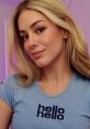 Young woman with blonde hair wearing a blue shirt displaying "hello" text, radiating a friendly vibe in soft lighting.