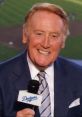 Vin Scully smiling, holding a Dodgers microphone, known for his legendary sports broadcasting career in baseball.