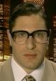 Peter O'Hanrahanrahan from Brass Eye looking serious, wearing large glasses and a beige suit against a city skyline background.