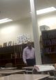 Teacher Douglas stands in a classroom, surrounded by bookshelves and student desks, engaging with the educational environment.