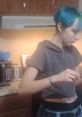 Person with teal hair preparing food in a cozy kitchen, showcasing a casual and creative home atmosphere.