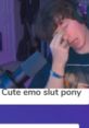 Person with dark, messy hair in a gaming setup, showing an exaggerated expression, with text below saying, "Cute emo slut pony.