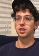 Greg from Supergenius Nerds looks contemplative while wearing a cap and glasses, seated against a casual background.
