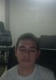 Casual portrait of a young man with short hair, sitting in front of a computer in a simple indoor space.