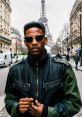 Stylish individual in a black and green jacket poses confidently near the Eiffel Tower, embodying urban fashion trends.