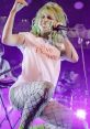 Hayley Williams performing on stage in a "Pure Pleasure" shirt, showcasing vibrant energy with fishnet leggings.