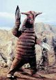 Gigantic Sadolar creature with a spiraled body and clawed hands stands in a rocky landscape, showcasing its unique design.
