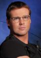 Daniel Jackson, portrayed by Michael Shanks, exudes confidence in a black tactical outfit with glasses on a blue backdrop.