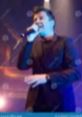 Rick Astley performing live on stage, passionately singing with a microphone under vibrant stage lights.