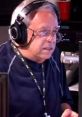 Larry Van Nuys speaking on air with headphones in a radio studio, focused on his broadcast and equipment.