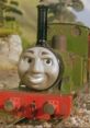 Smudger from Thomas the Tank Engine grins brightly, showcasing his green locomotive design in a lush, scenic backdrop.