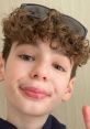 Cheerful young boy with curly hair and sunglasses giving a peace sign, showcasing a playful personality. Perfect for Daniell!