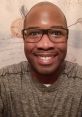 Smiling man in glasses wearing a gray shirt, with a decorative background, exuding a friendly and welcoming vibe.