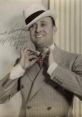 Max Miller, dressed in a stylish suit and fedora, adjusting his tie with a confident smile, capturing vintage elegance.