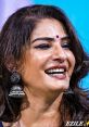Raveena Tandon smiles brightly, showcasing her elegant earrings and gorgeous makeup at a vibrant event.
