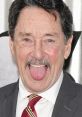 Peter Cullen playfully sticking out his tongue, showcasing his cheerful personality in a professional suit and tie.