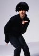 Jay Kay striking a playful pose, showcasing his unique fashion sense and style. Iconic look with bold hat choice.
