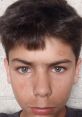 Young boy with short dark hair and striking blue-green eyes, displaying a serious expression against a textured background.