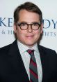 Matthew Broderick smiles at a red carpet event, showcasing his signature glasses and stylish attire, exuding charm and elegance.
