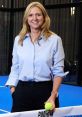 Gigi Salmon smiles confidently, holding a tennis ball in a vibrant blue court setting while wearing a casual light shirt.