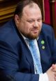 Ruslan Stefanchuk in a formal setting, wearing a blue suit and patterned tie, engaged in discussion at a parliamentary session.