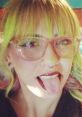 Person with colorful hair and glasses sticking out tongue, showcasing a playful and trendy style.