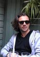 Young man with long hair and sunglasses, relaxing at a café setting, exuding a stylish and casual vibe.