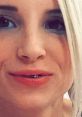 Close-up of a woman with light hair and unique dental jewelry, showcasing her vibrant makeup and confident smile.