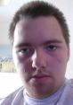 Portrait of a young man with short hair and a neutral expression, softly lit indoor setting.
