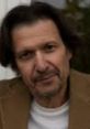 Luca Sandri with a thoughtful expression, wearing a beige jacket, against a blurred background.