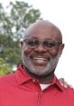 Smiling man in red shirt with glasses, showcasing a friendly demeanor outdoors, representing warmth and approachability.